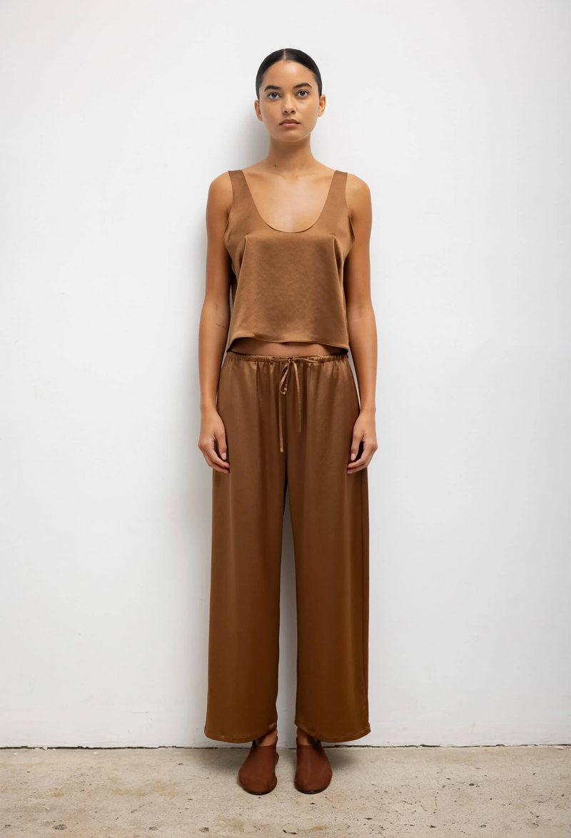 A woman wearing a loose brown tank top and matching pants. White background.
