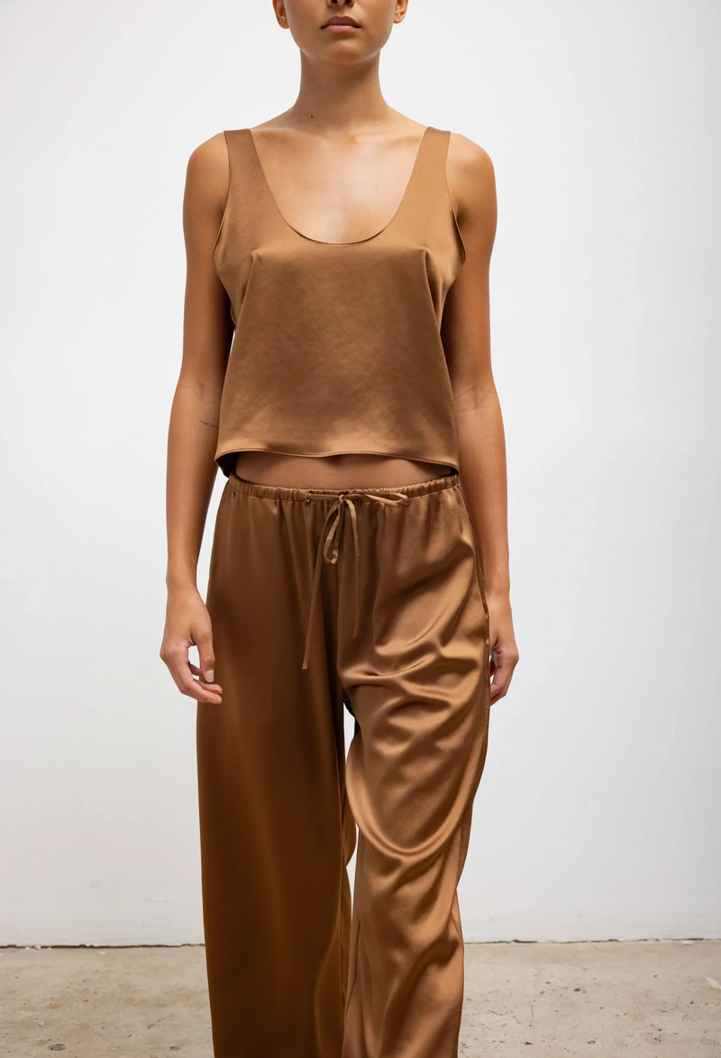 A woman wearing a loose brown tank top and matching pants. White background.