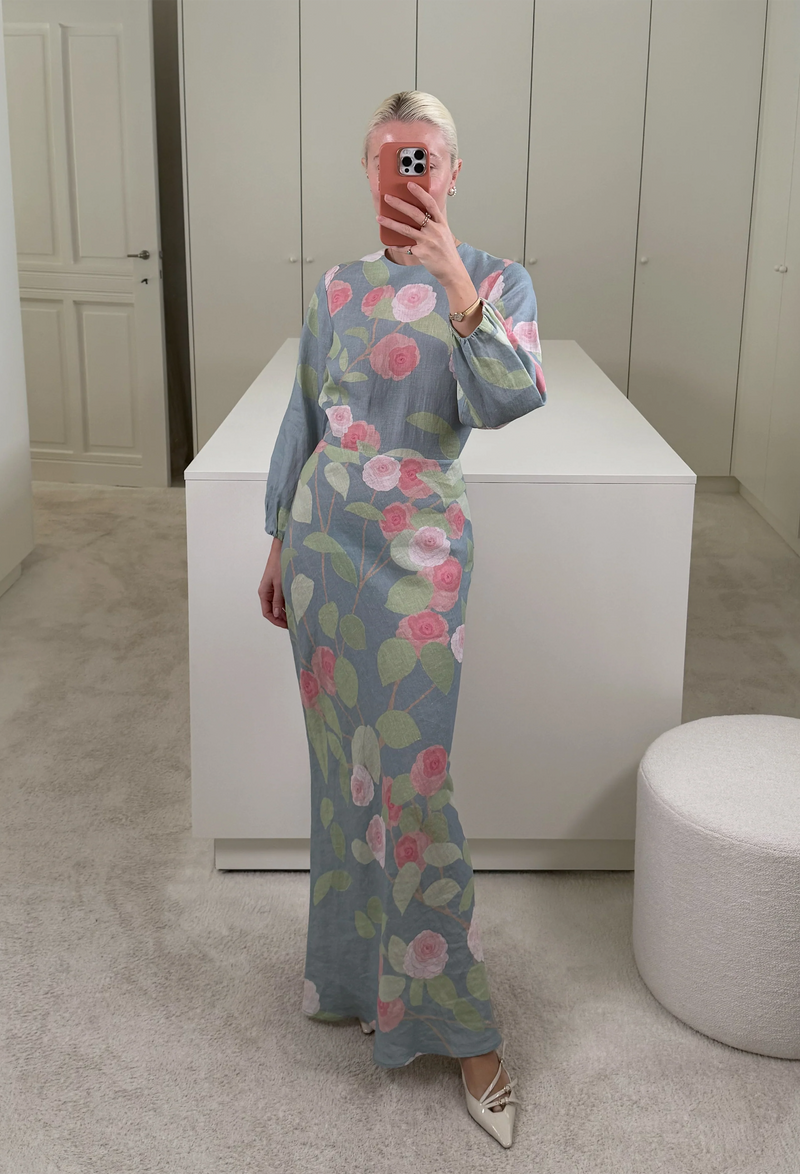 A woman in a closet taking a mirror selfie wearing a blue dress with long sleeves and pink and red roses on it.