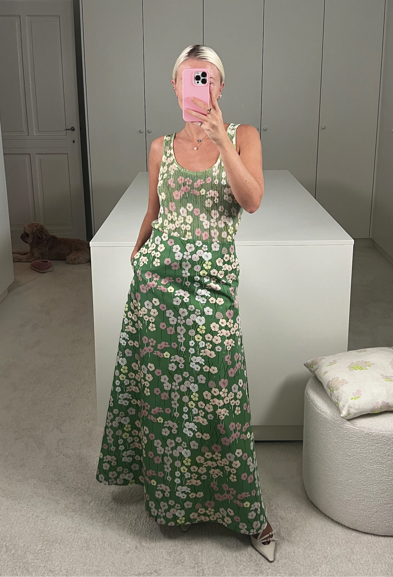 A woman in a closet taking a mirror selfie wearing a long green skirt with a pastel colored flowers print and a matching tank top.