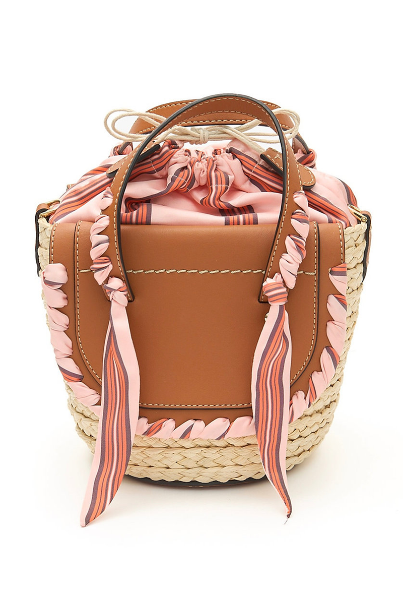 The back of a mini basket bag with leather flaps, pink ribbon detailing, and two small leather handles and a crossbody strap. Transparent background.