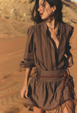 A woman in the desert wearing a matching brown button down shirt and skirt with lace detailing and leather belt.