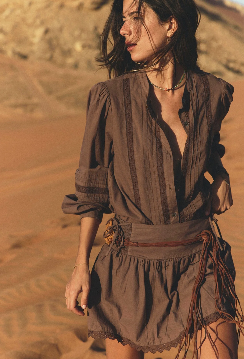 A woman in the desert wearing a matching brown button down shirt and skirt with lace detailing and leather belt.