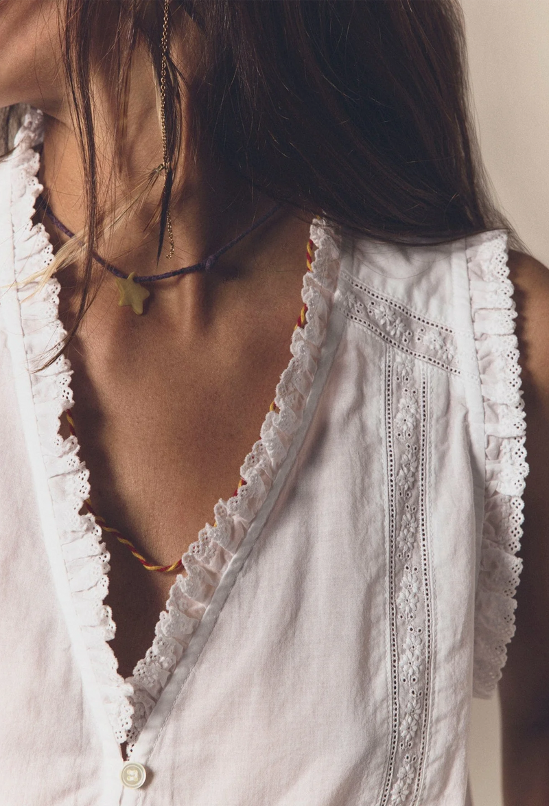 Close up of the neck of a woman wearing a sleeveless white button down top. Beige background.