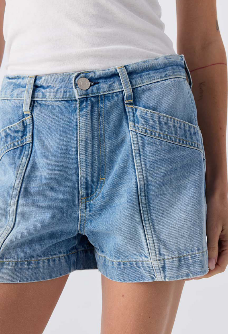 Close up of a woman wearing a white tank top and blue jean shorts. Taken on a white background.