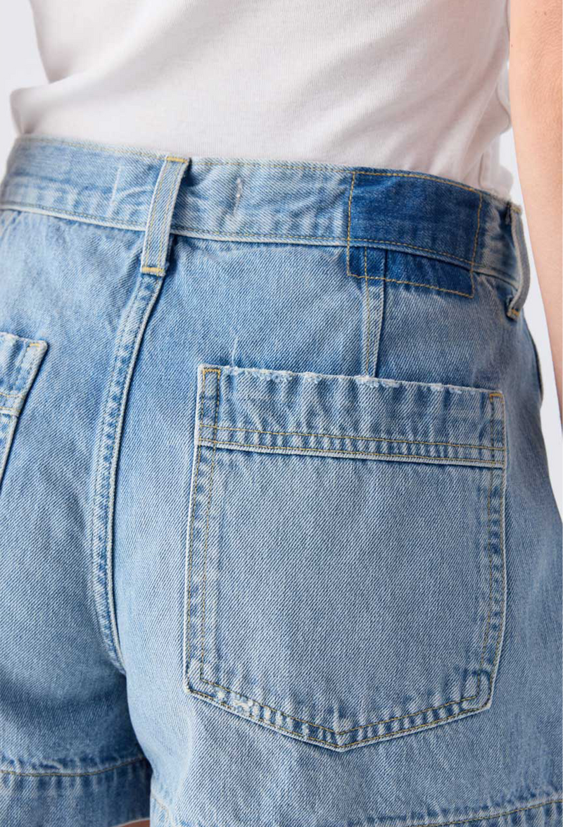 Close up of the back of a woman wearing a white tank top and blue jean shorts. Taken on a white background.