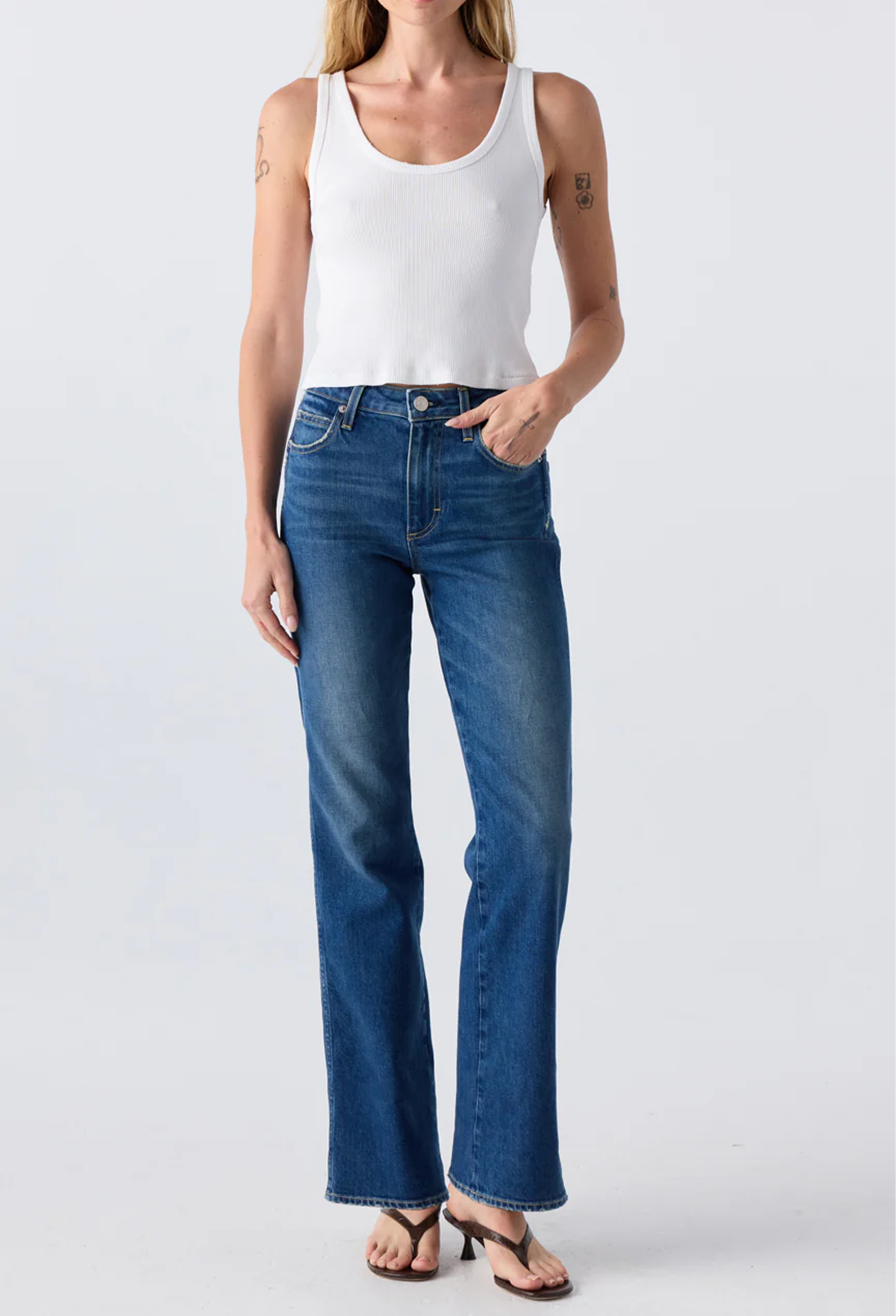 Close up of a woman wearing a white tank top and blue jeans. Taken on a white background.