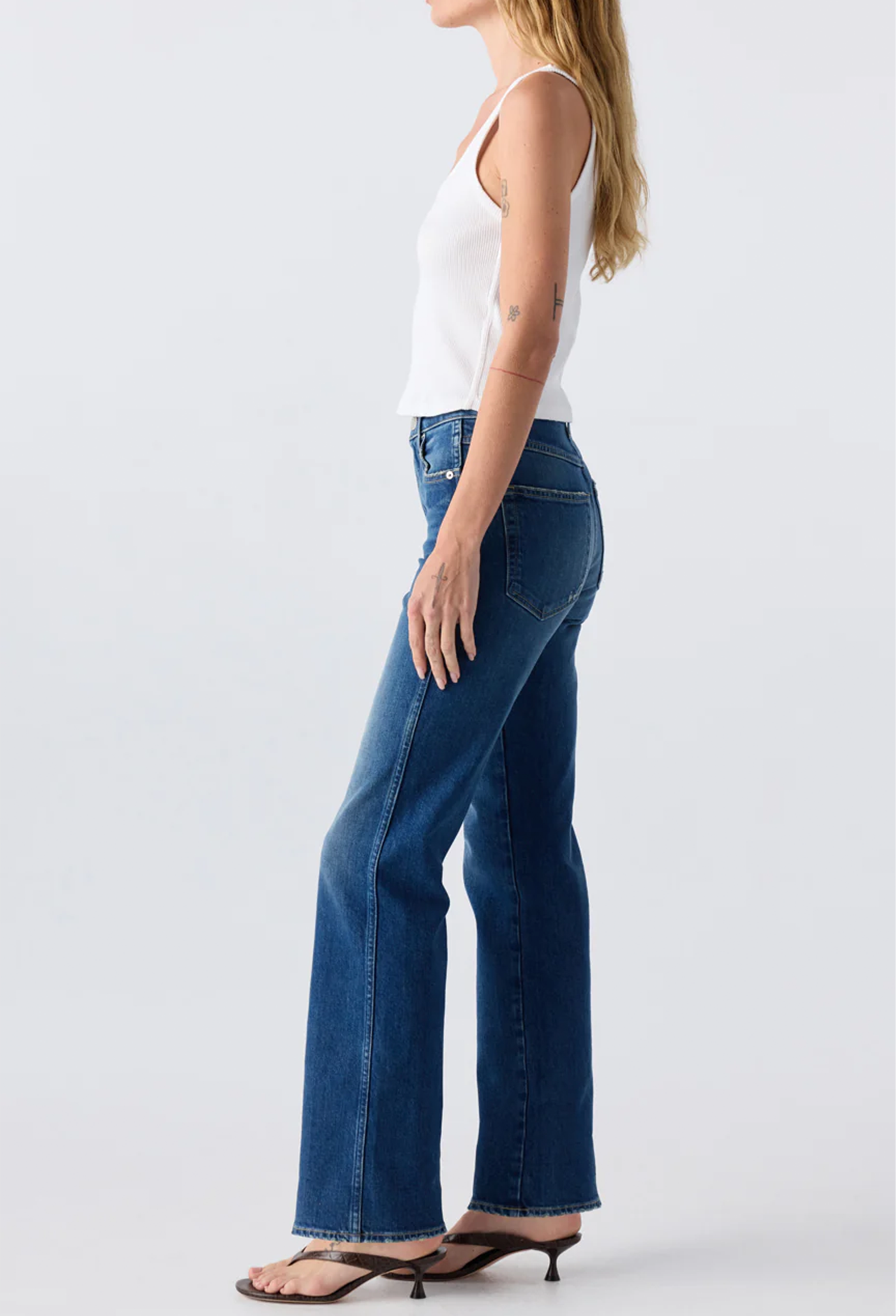 The side of a woman wearing a white tank top and blue jeans. Taken on a white background.