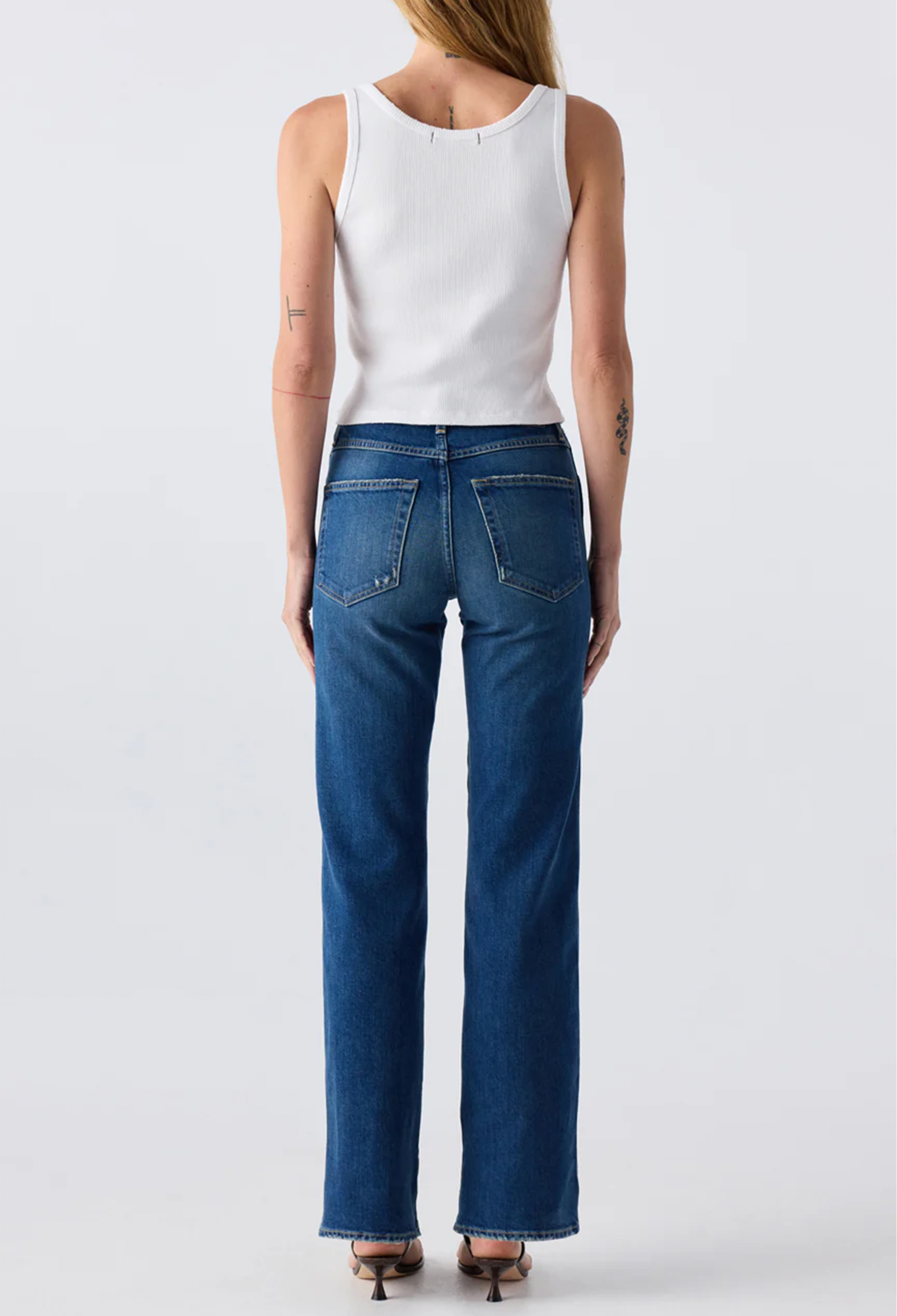 The back of a woman wearing a white tank top and blue jeans. Taken on a white background.