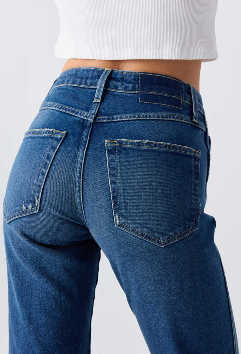 Close up of the back pockets of a woman wearing a white top and blue jeans. Taken on a white background.