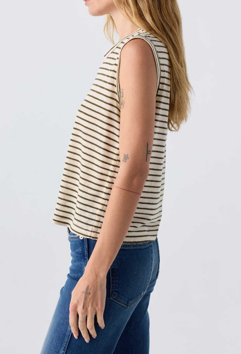 Close up of the side of a woman wearing jeans and an off white sleeveless tee with brown stripes. Taken on a white background.