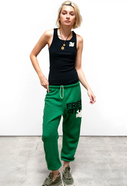 A woman wearing a black tank top and green sweatpants with free city printed in black lettering next to a white dove. Taken on a white background.
