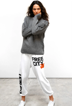 A woman wearing white sweatpants with letsgo and free city printed in black lettering next to an orange dove graphic. Taken on a white background.