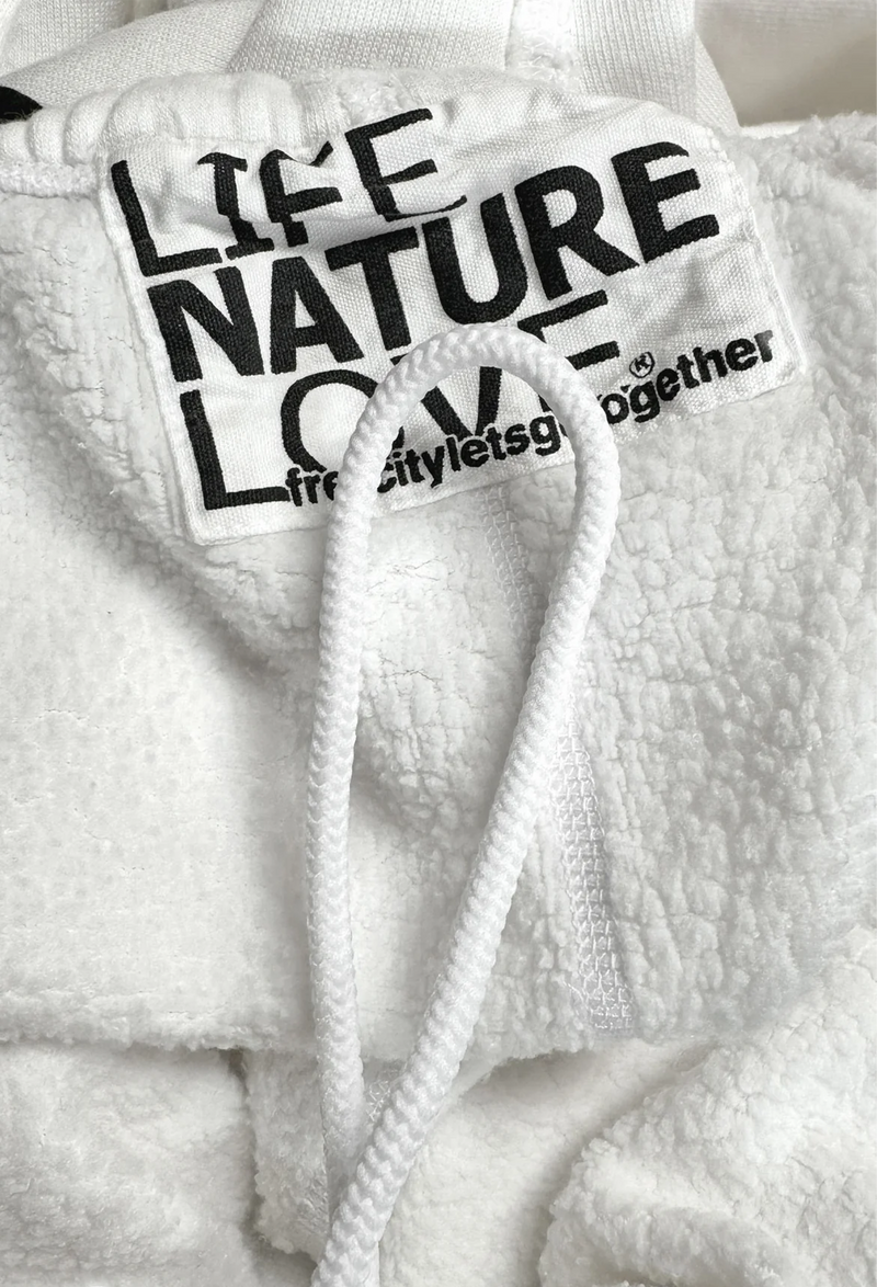 Detail shot of the tag on white sweatpants that reads life nature love free city lets go together next to the drawstring.