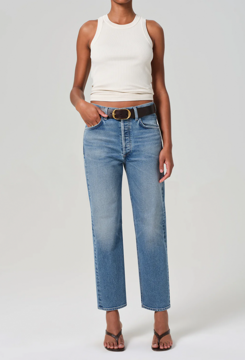 Model wears form fitting ribbed racerback white tank. She also wears blue jeans, a brown belt, and brown sandals. 