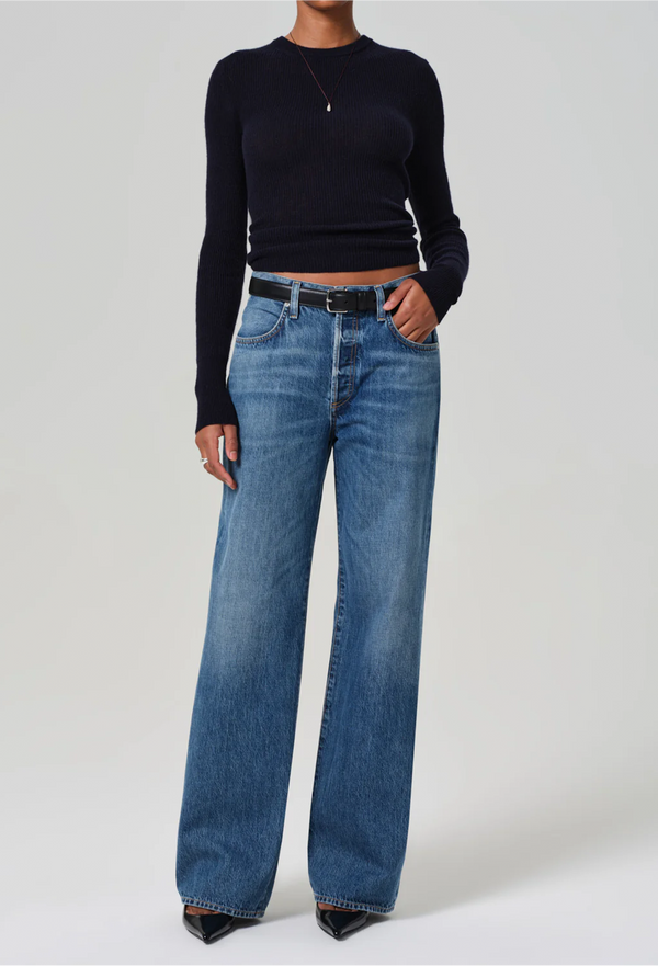 Model wears wide leg dark wash blue jeans with a black sweater, black belt, and black heels.