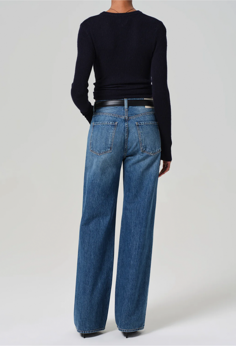 From behind, model wears wide leg dark wash blue jeans with a black sweater, black belt, and black heels.