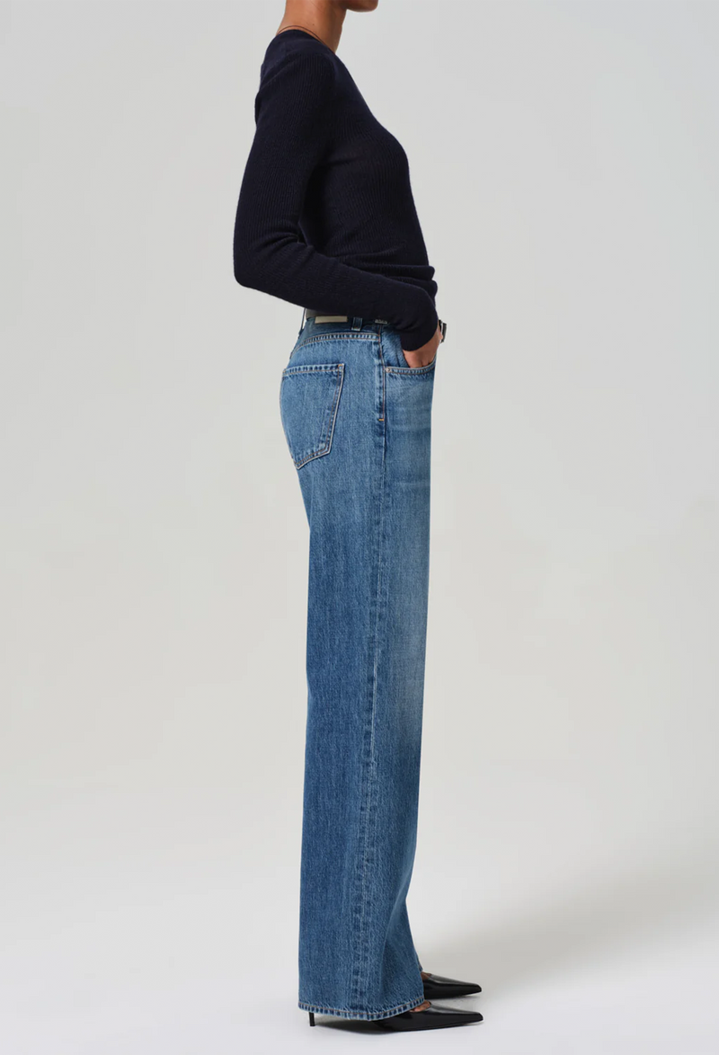 Facing the right side, model wears wide leg dark wash blue jeans with a black sweater, black belt, and black heels.