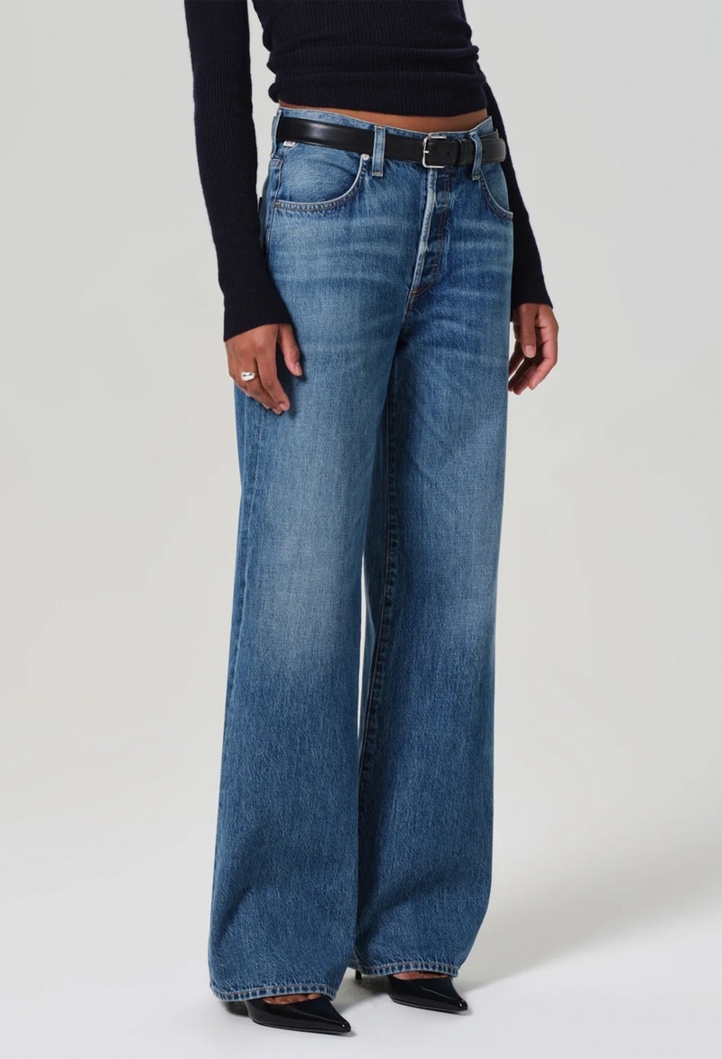 Model wears wide leg dark wash blue jeans with a black sweater, black belt, and black heels.