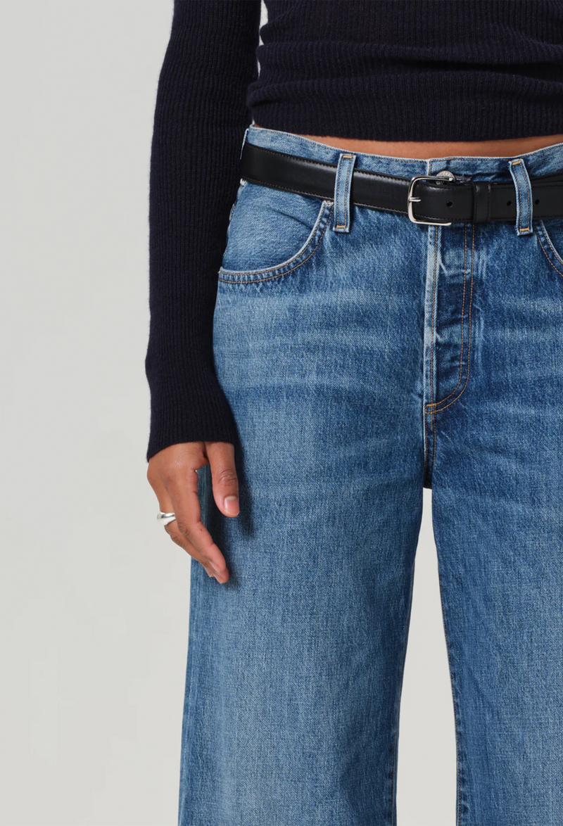 Model wears wide leg dark wash blue jeans with a black sweater, with black belt.