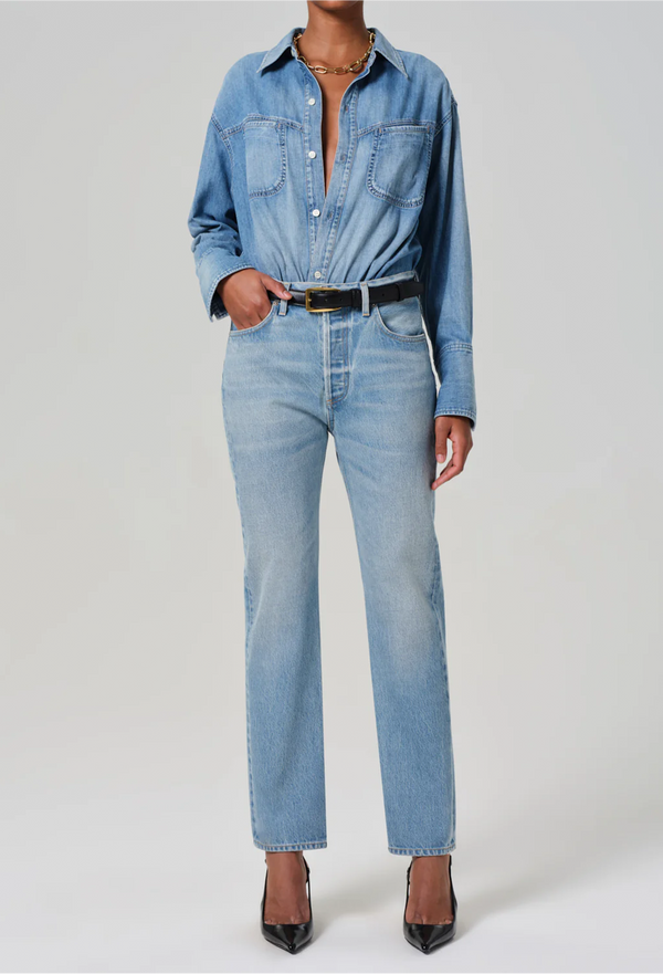 Model wears high rise jeans with denim button down shirt. She also wears black heels, a black belt, and a gold necklace. 