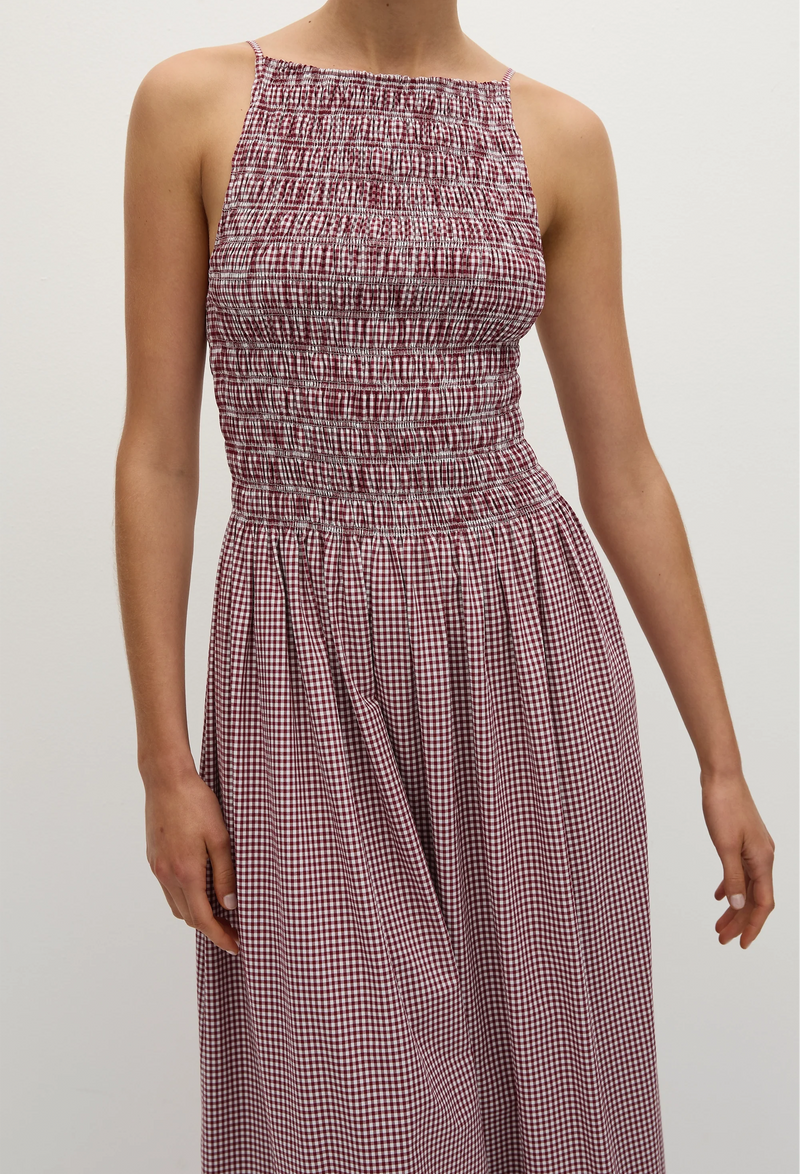 A close up of a woman wearing a red and white gingham printed midi dress with a shirred bodice and rounded neckline. Taken on a white background.
