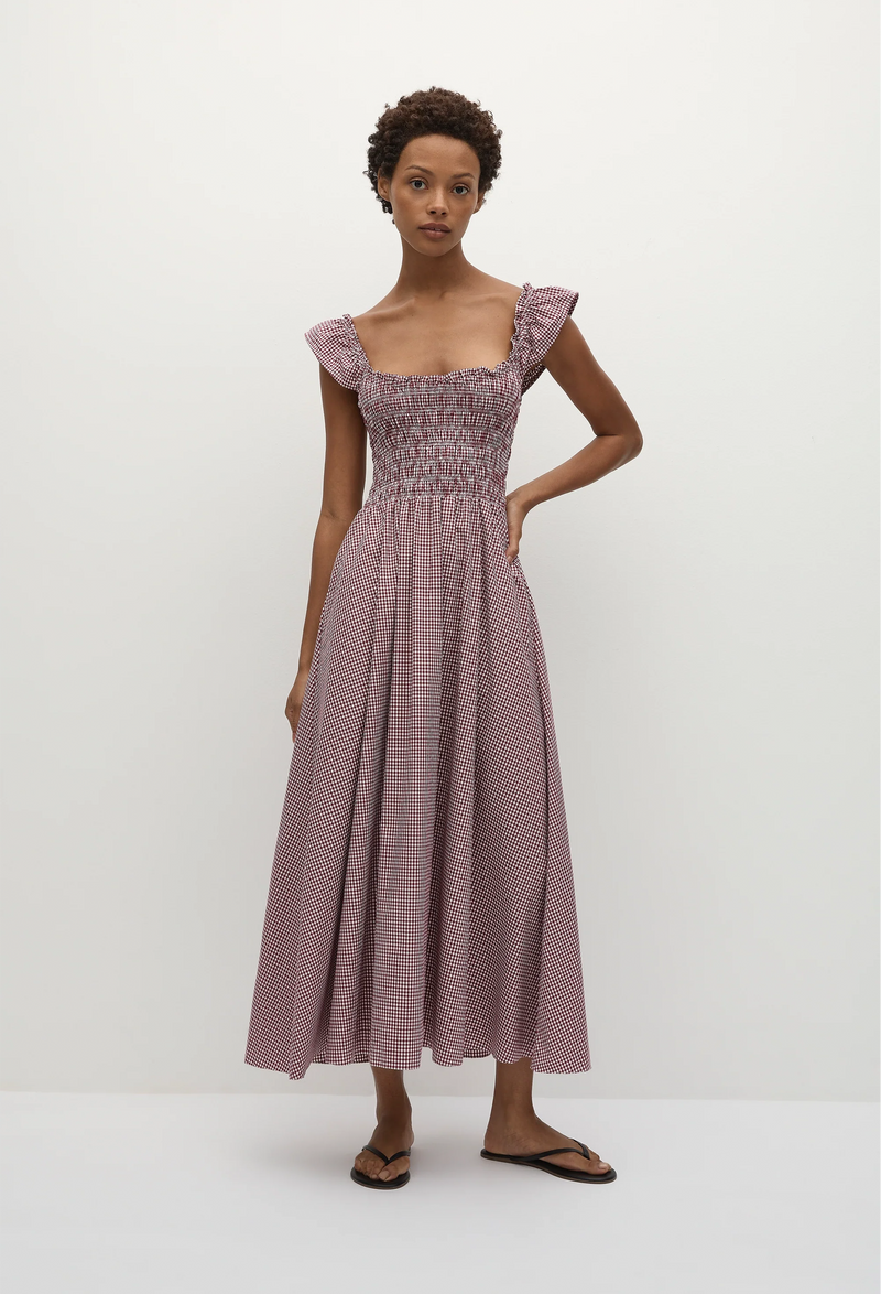 Short-haired woman wearing a red and white gingham print midi dress with short flutter sleeves and a shirred bodice. Taken on a white background.