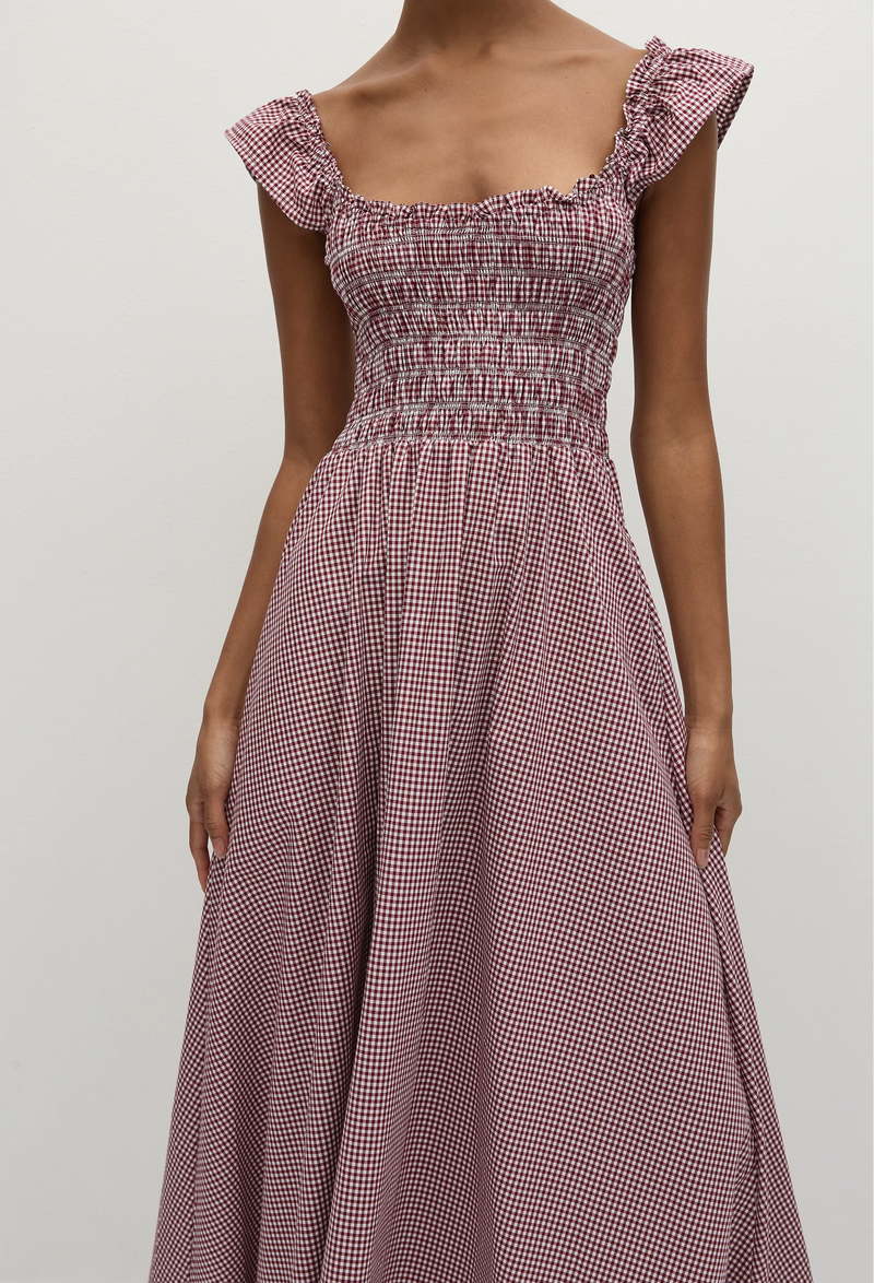 Close-up of a woman wearing a red and white gingham print midi dress with short flutter sleeves and a shirred bodice. Taken on a white background.