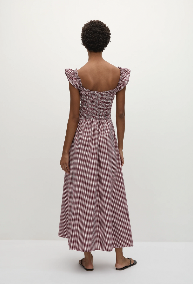 The back of a short-haired woman wearing a red and white gingham print midi dress with short flutter sleeves and a shirred bodice. Taken on a white background.