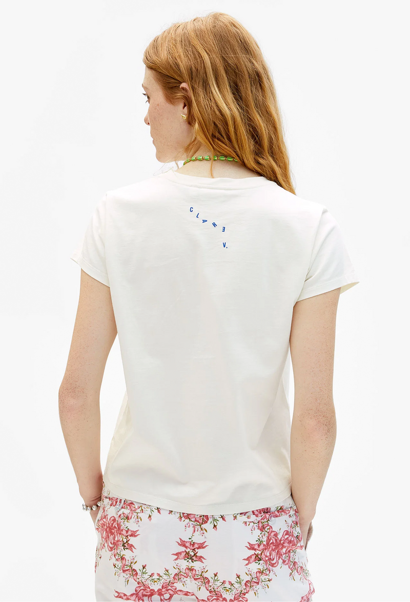 Woman wearing a white tee shirt with CLARE V. printed in blue lettering on the back. On a white background