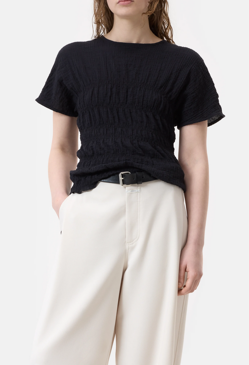 Model wears textured crinkled short sleeve black top with wide leg cream pants and a black belt. 