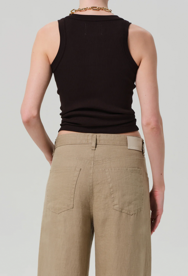 From behind, model wears form fitting ribbed racerback chocolate brown tank. She also wears khaki drawstring pants, and a gold necklace. 