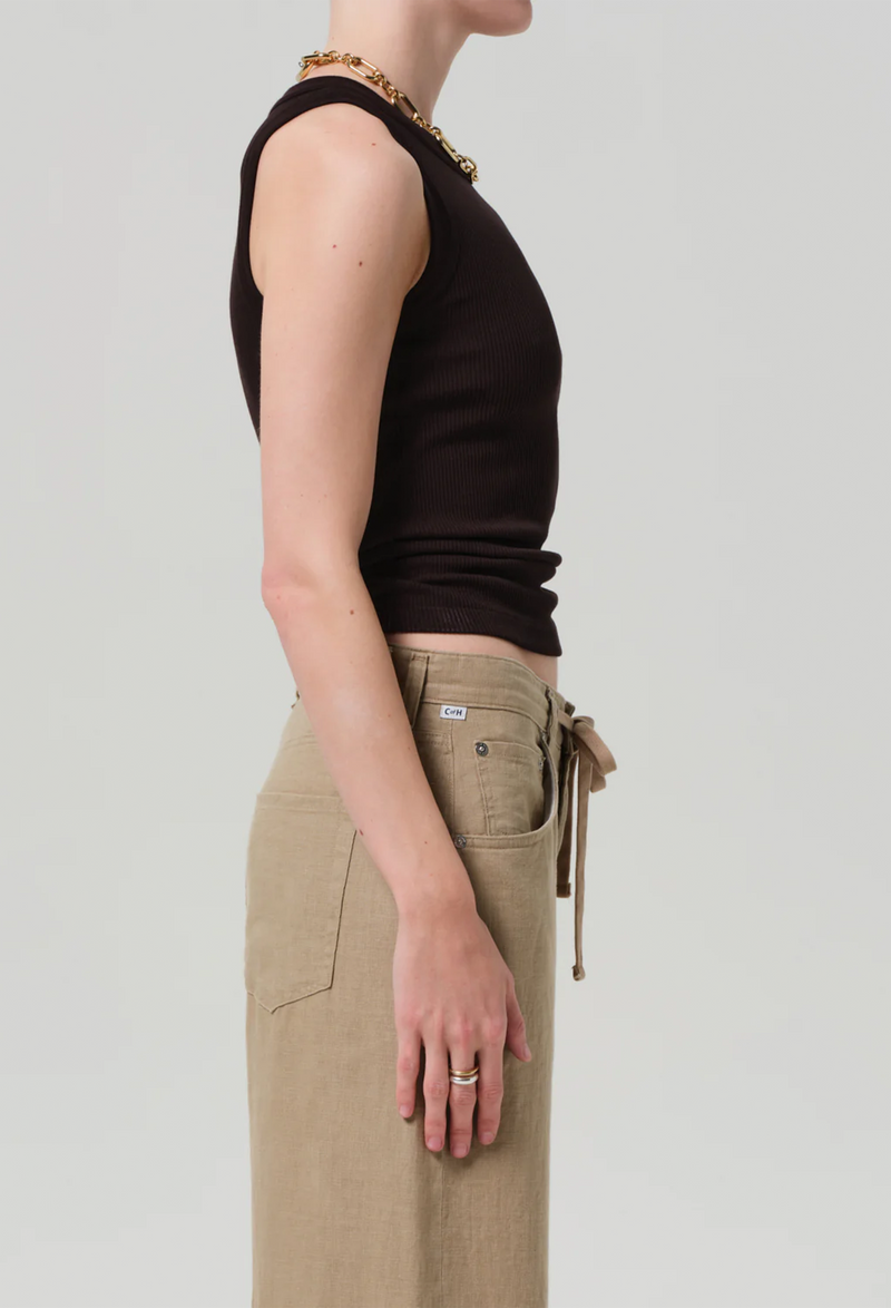 Facing the right side, model wears form fitting ribbed racerback chocolate brown tank. She also wears khaki drawstring pants, and a gold necklace. White background.