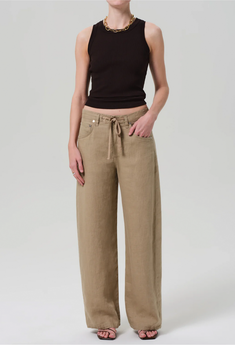 Model wears form fitting ribbed racerback chocolate brown tank. She also wears khaki drawstring pants, a gold necklace, and black sandals. White background.