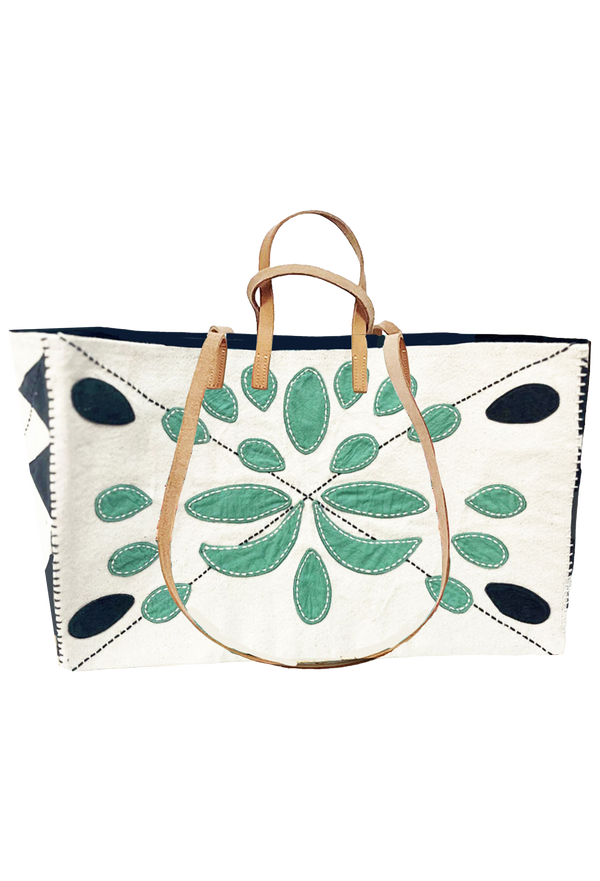 Large white tote, black embroidered ovals on all four corners of back, with green embroidered ovals in the middle. Also includes long tan handles for shoulder, and short handles for carrying. Set against a checkered background.