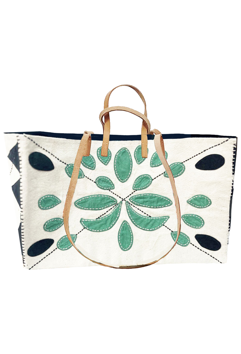 Large white tote, black embroidered ovals on all four corners of back, with green embroidered ovals in the middle. Also includes long tan handles for shoulder, and short handles for carrying. Set against a checkered background.