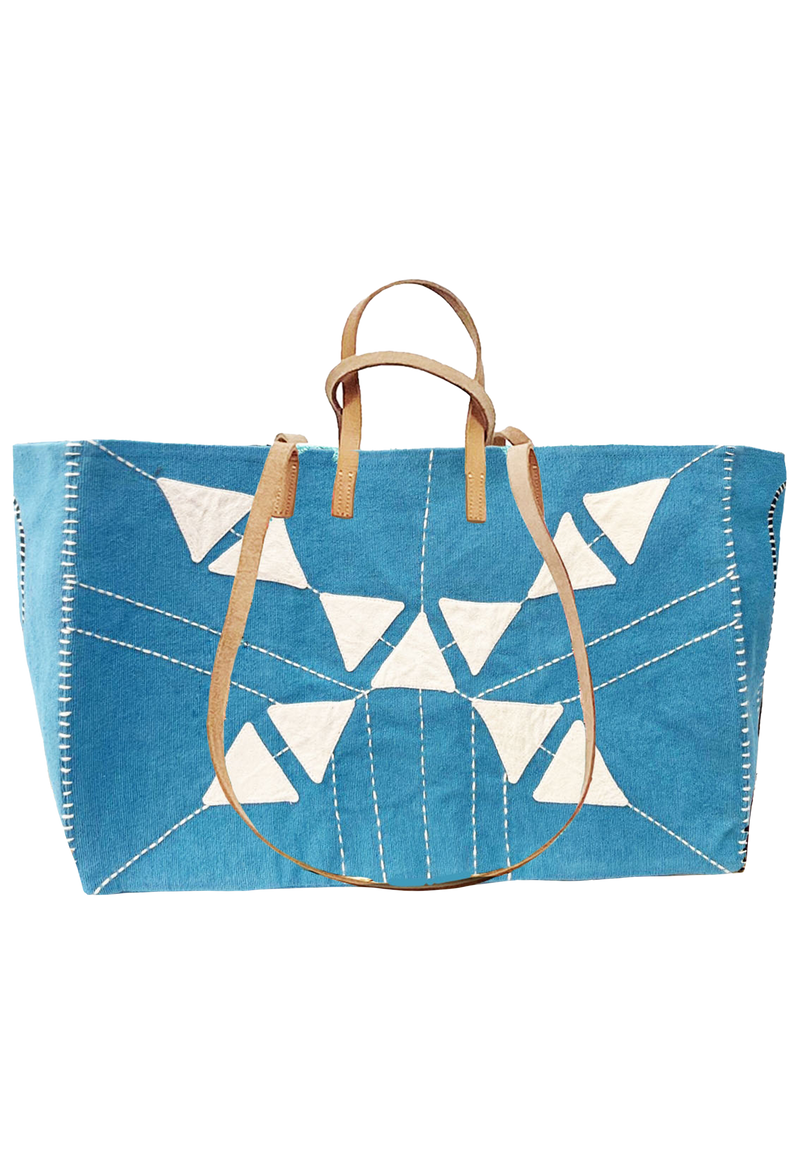 Large blue tote with white stitching going towards the middle. Embroidered triangular shapes in the center. Long and short tan handles.