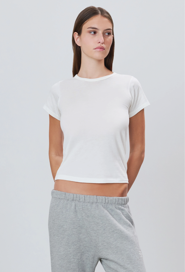 a woman wearing a white short sleeve fitted t-shirt and grey sweatpants. white background.