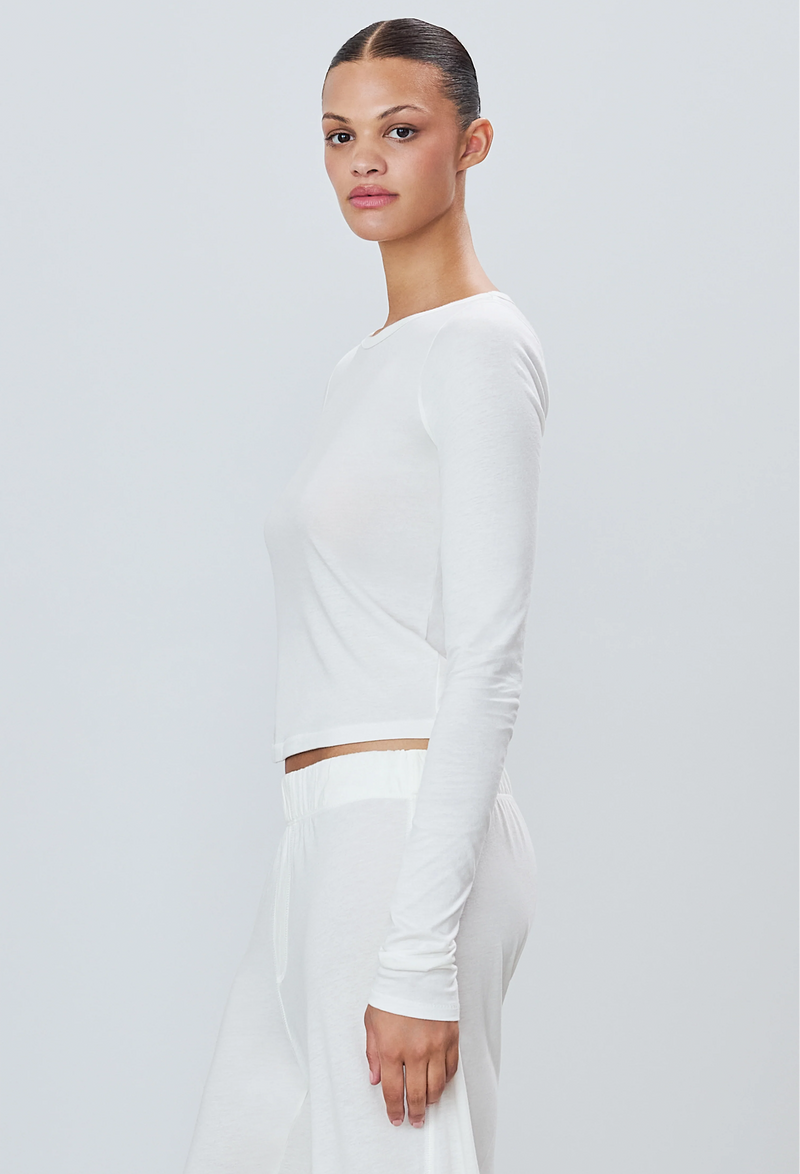 a woman wearing a white long sleeve fitted t-shirt and white sweatpants. white background.