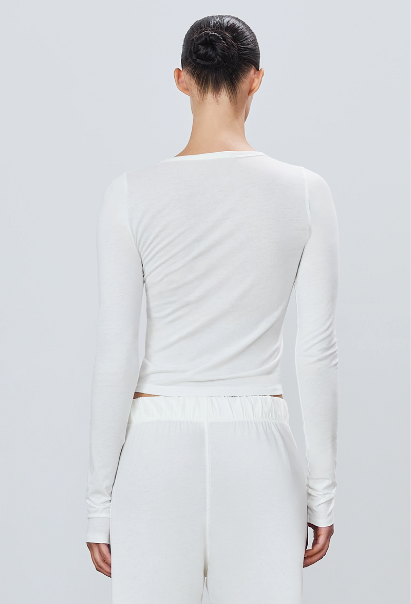 the back of a woman wearing a white long sleeve fitted t-shirt and white sweatpants. white background.