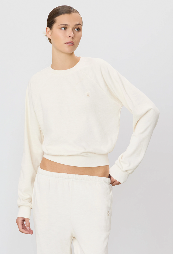 a woman wearing an off-white raglan sweatshirt and sweatpants. white background.
