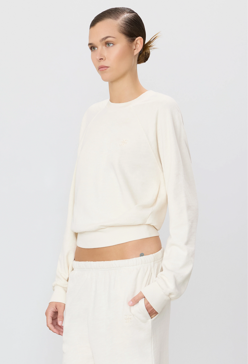 a woman wearing an off-white raglan sweatshirt and sweatpants. white background.