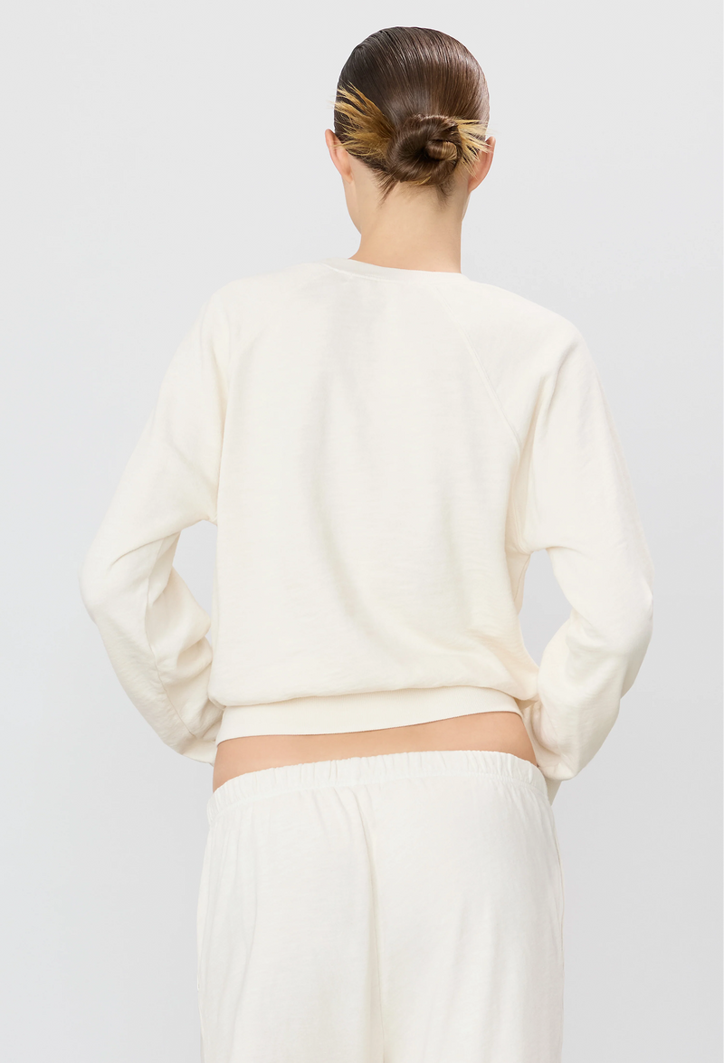 the back of a woman wearing an off-white raglan sweatshirt and sweatpants. white background.