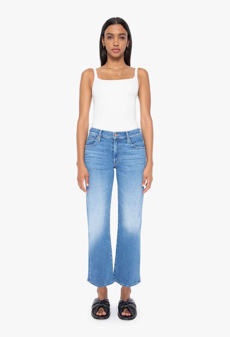 a woman wearing a white tank top and blue jeans cropped at the ankle. white background
