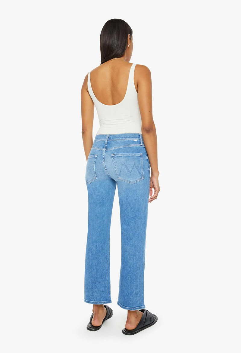 the back of a woman wearing a white tank top and blue jeans cropped at the ankle. white background