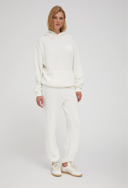 a woman wearing an off white hoodie with a white heart printed on the breast and matching sweats. white background