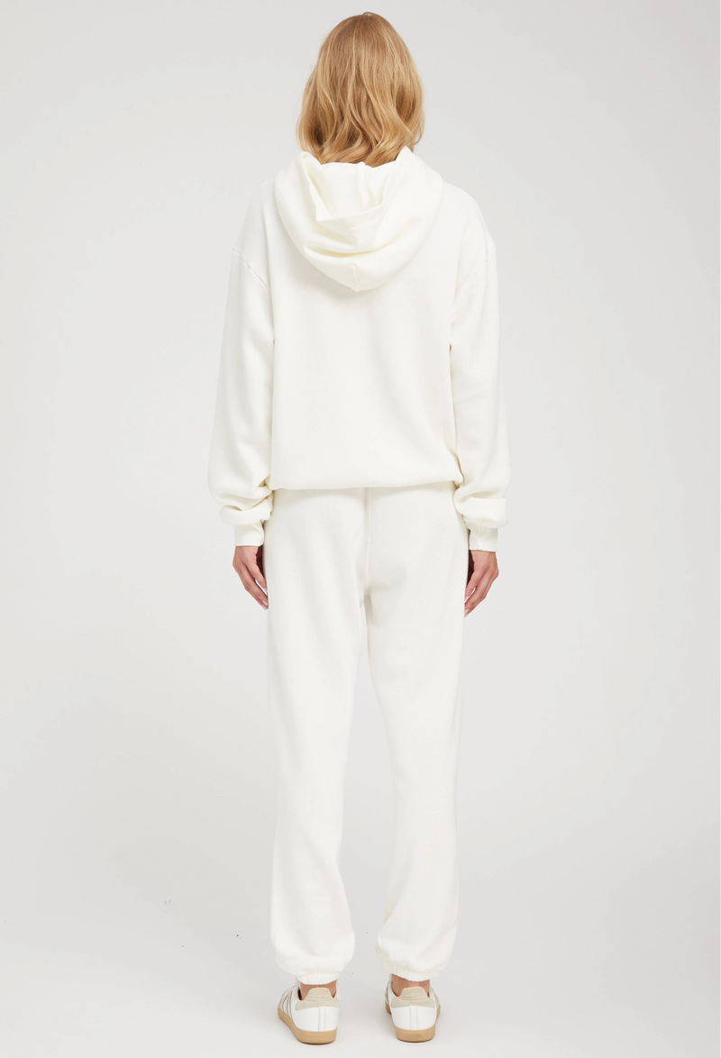 the back of a woman wearing an off white hoodie with matching sweats. white background