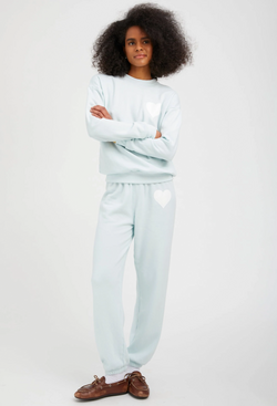 a woman wearing a pastel icy blue sweatshirt with a white heart printed on the breast with matching sweatpants. white background