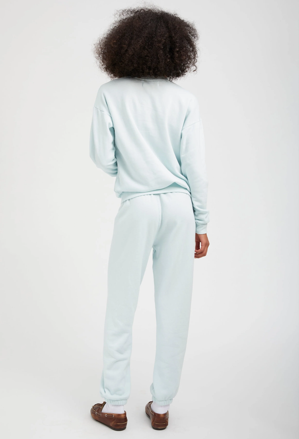 the back of a woman wearing a pastel icy blue sweatshirt with matching sweatpants. white background