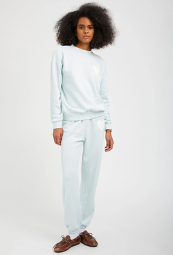 a woman wearing a pastel icy blue sweatshirt with a white heart printed on the breast with matching sweatpants. white background